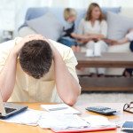 Man calculating his bills while his family are on the sofa