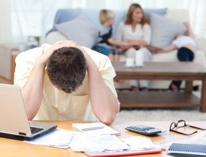 Man calculating his bills while his family are on the sofa