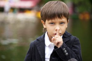 Young beautiful Little Boy has put forefinger to lips as sign of silence