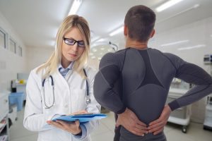 Man patient suffering from back pain during medical exam by doctor