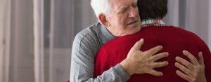 Older grateful man hugging his helpful caregiver